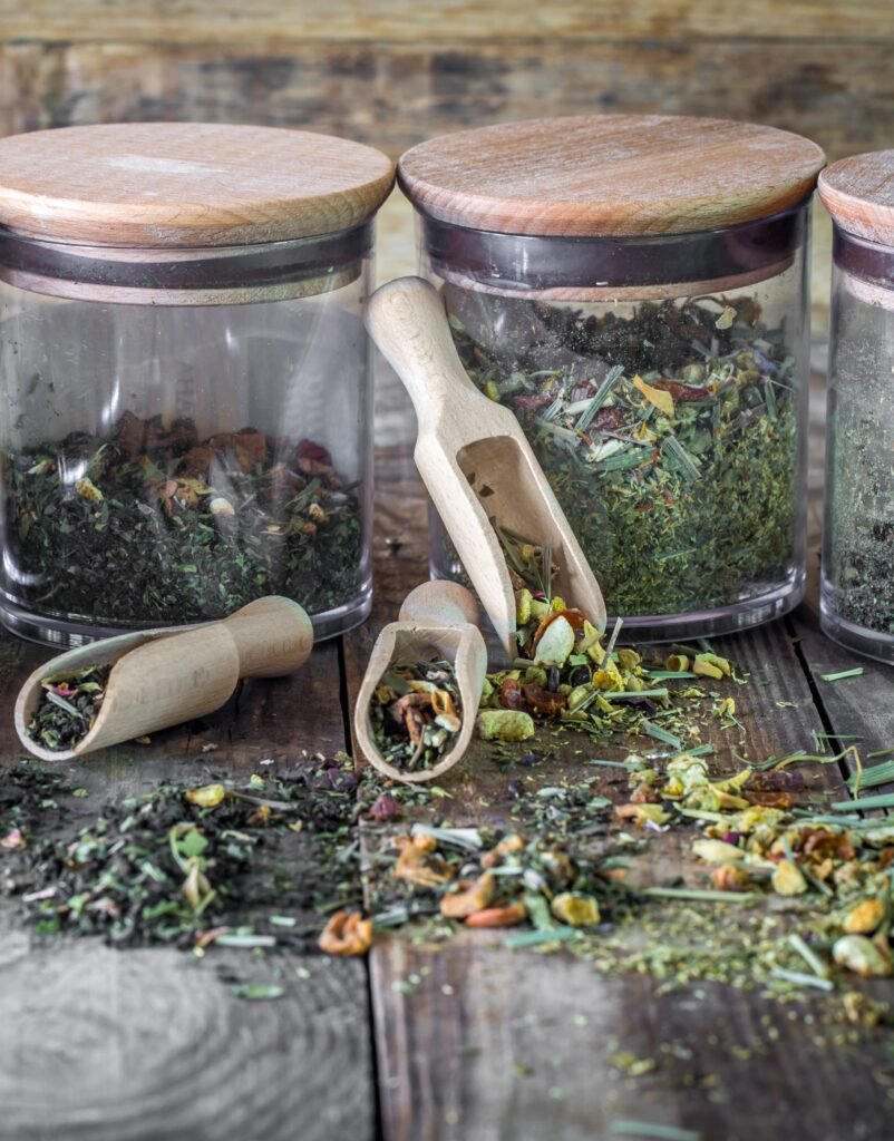 still life of loose tea in glass jar and wooden spoons on wooden background